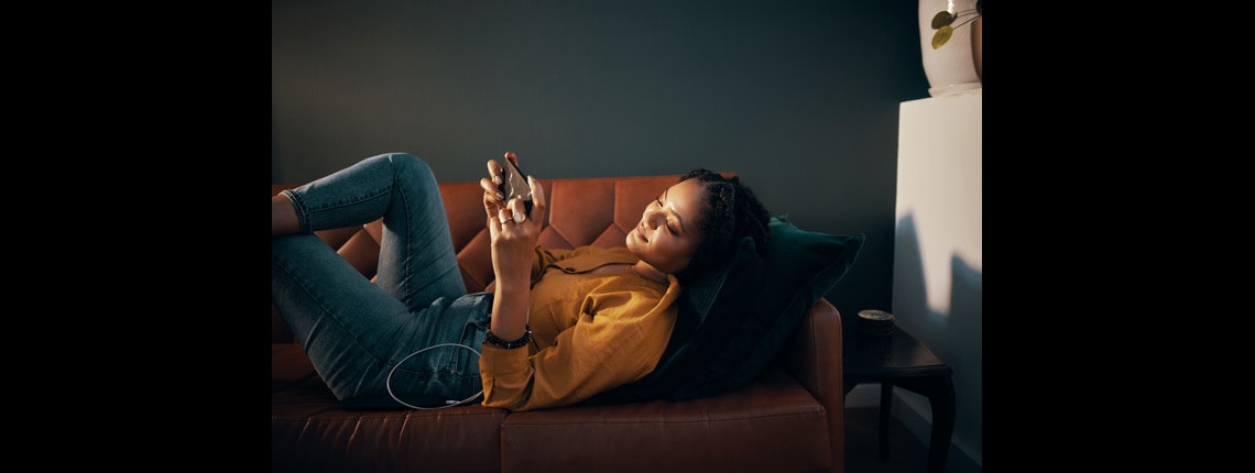 A woman laying on the couch holding a device.